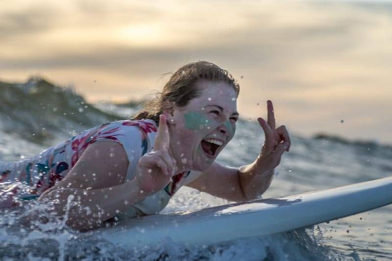A beginner lying on her surfboard laughing at sunset during a lesson in Weligama