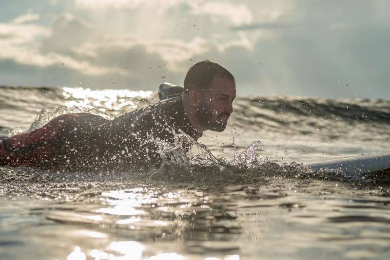 A surfer paddling out through backlit spray at Weligama