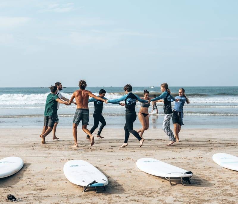 Guests warming up together on the beach before a surf lesson, boards lined up on the sand at Weligama, Sri Lanka