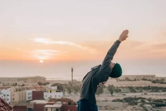 Sunset yoga stretch on a rooftop overlooking Tamraght and the Atlantic, Morocco