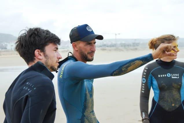 A surf coach pointing out the conditions to two students on the beach at Tamraght, Morocco