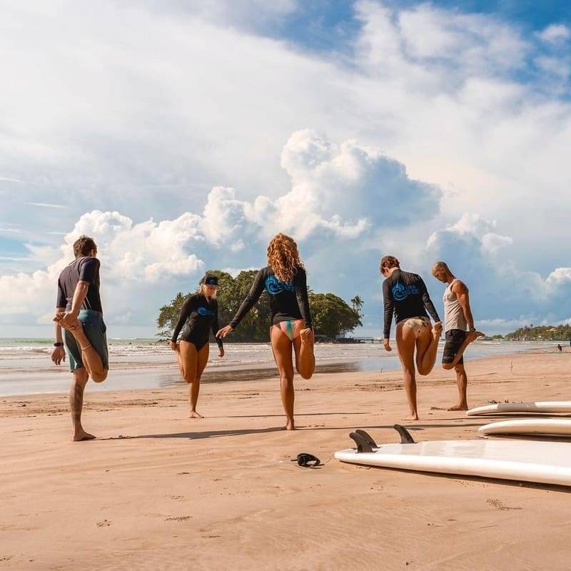 Guests stretching on the beach beside their boards before a surf session at Weligama, Sri Lanka